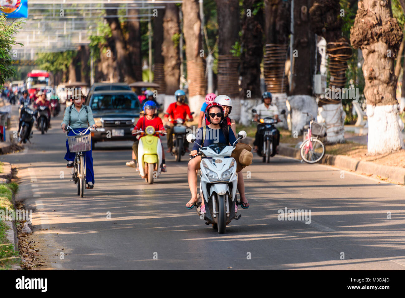 People riding scooters, bicycles and driving cars along a road in Siem Reap, Cambodia. Stock Photo