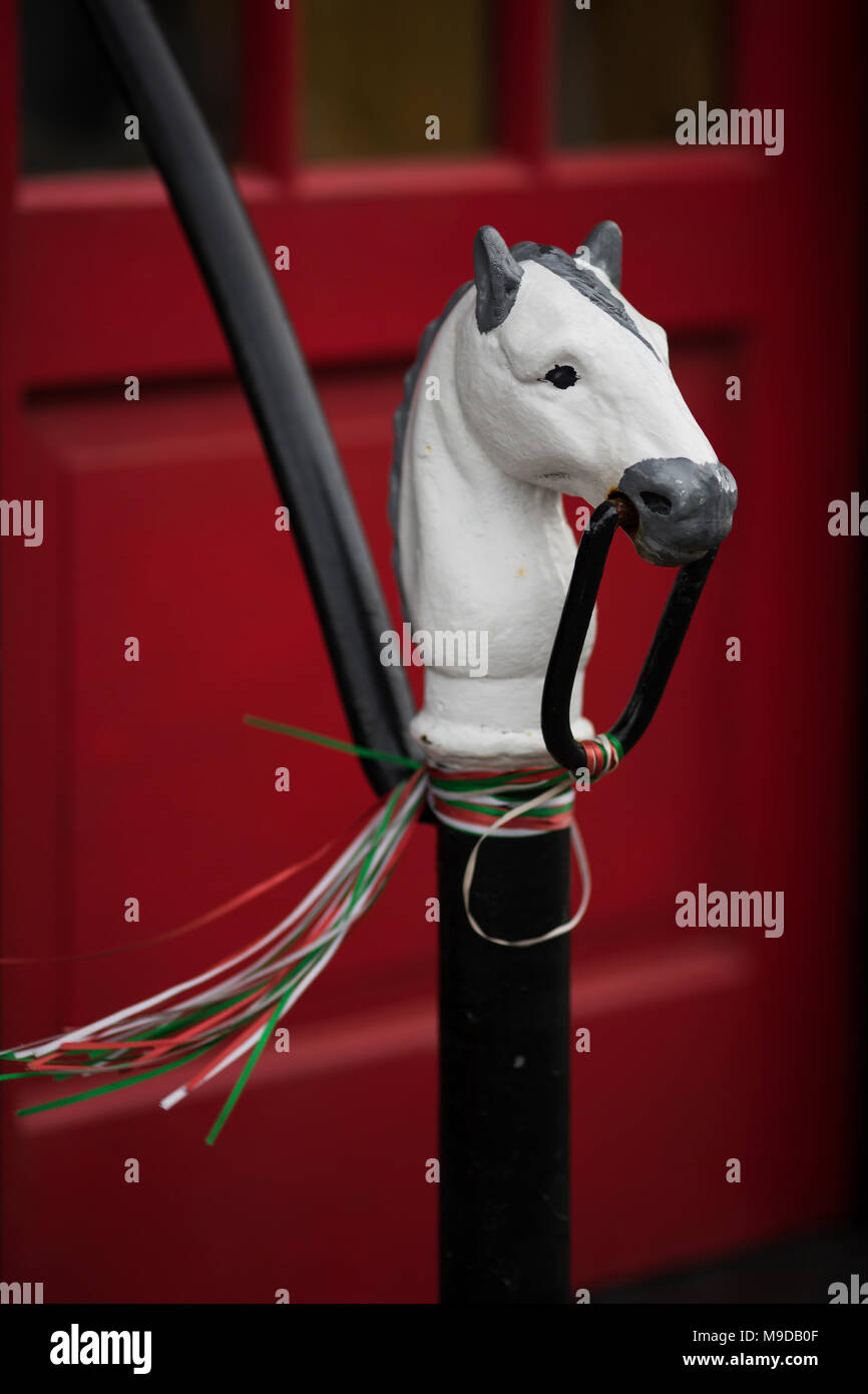 A painted horse hitching post tied with ribbon streamers in front of a red door in Rockport, Massachusetts, USA. Stock Photo