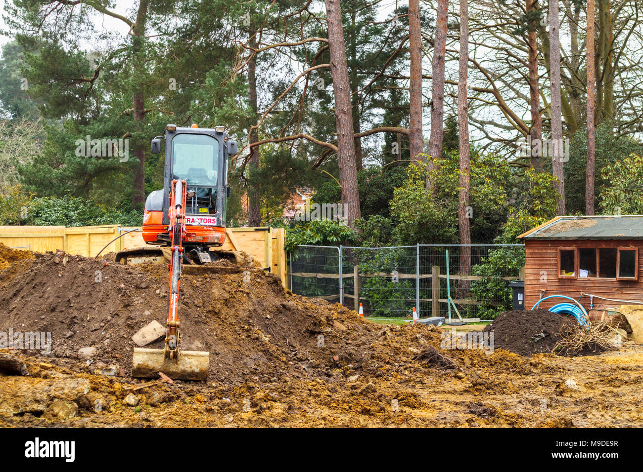 Large orange heavy plant mechanical digger parked on top of a mound of earth on a new suburban residential development construction site Stock Photo