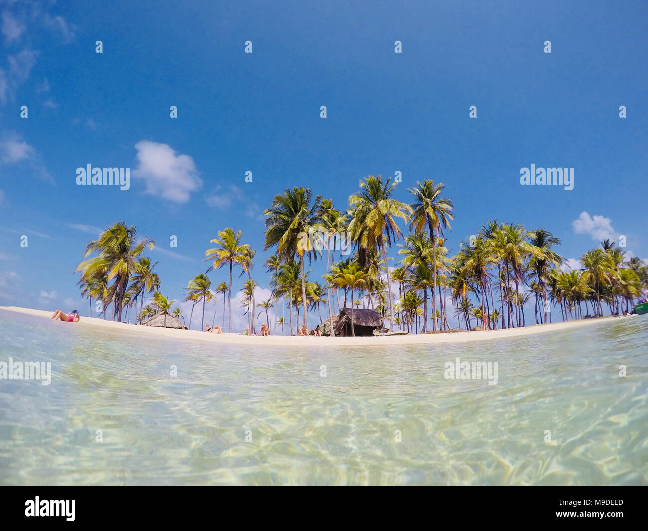 summer time  - people on small island relaxing on beach below palm trees Stock Photo
