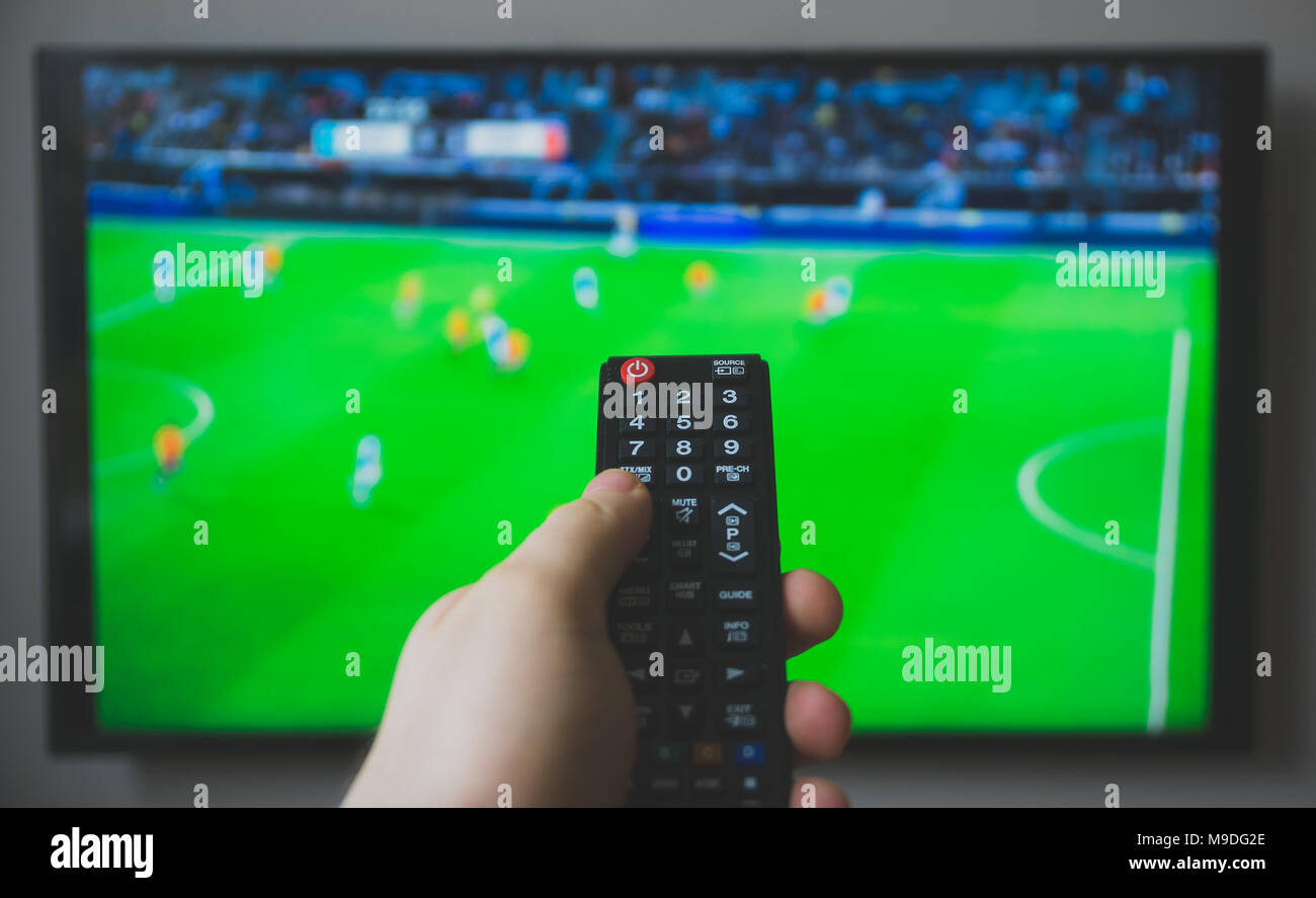Male hand holding TV remote control. Football game. Stock Photo