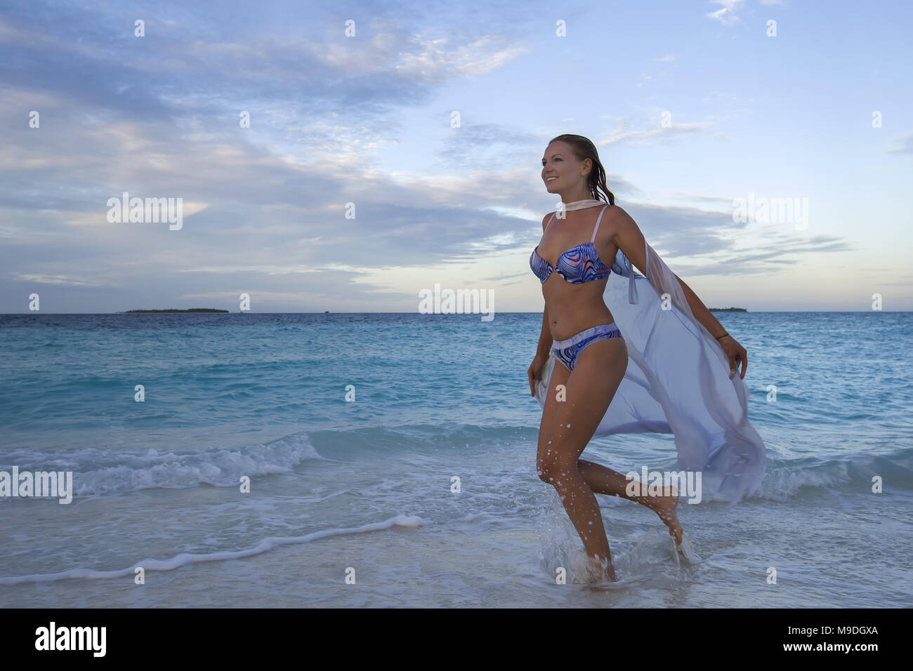 Young woman in bikini runs on water at sunset Stock Photo
