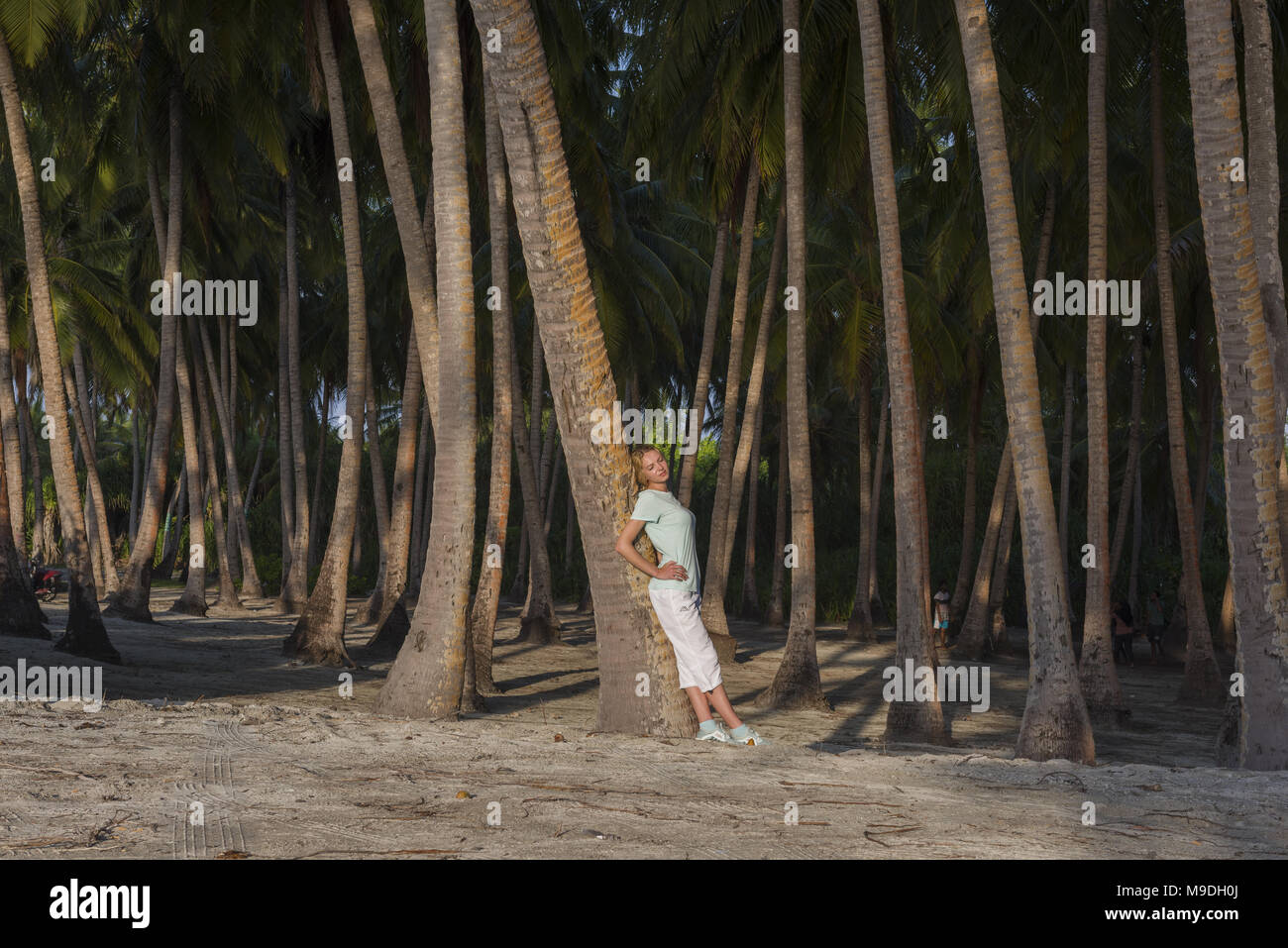 Young beautiful woman standing in a tropical forest leaning on a palm tree Stock Photo