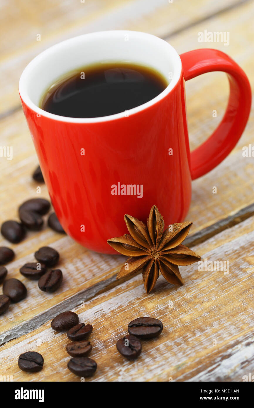 Star anise leaning against red mug of black coffee on rustic wooden surface Stock Photo