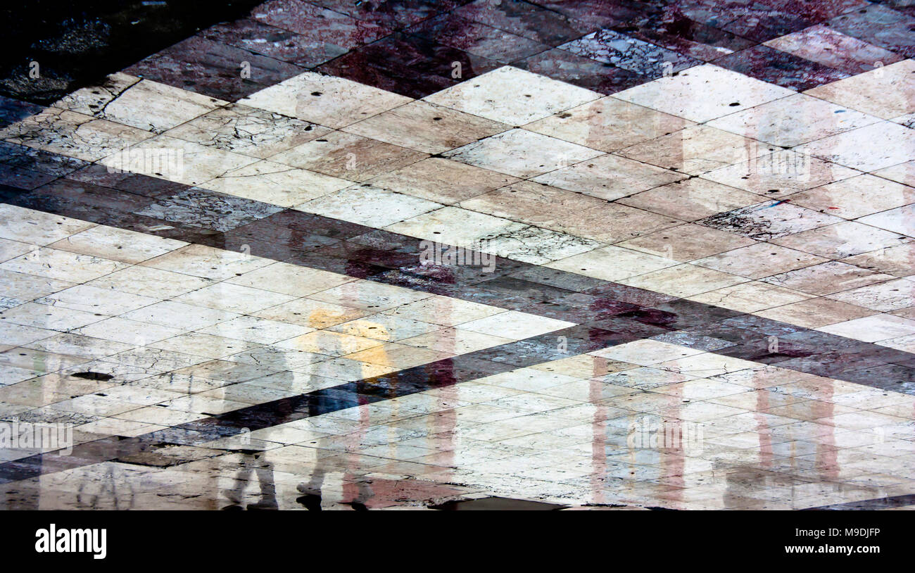 Abstract wet shiny geometrical city square pavement reflecting buildings and people on a rainy day Stock Photo