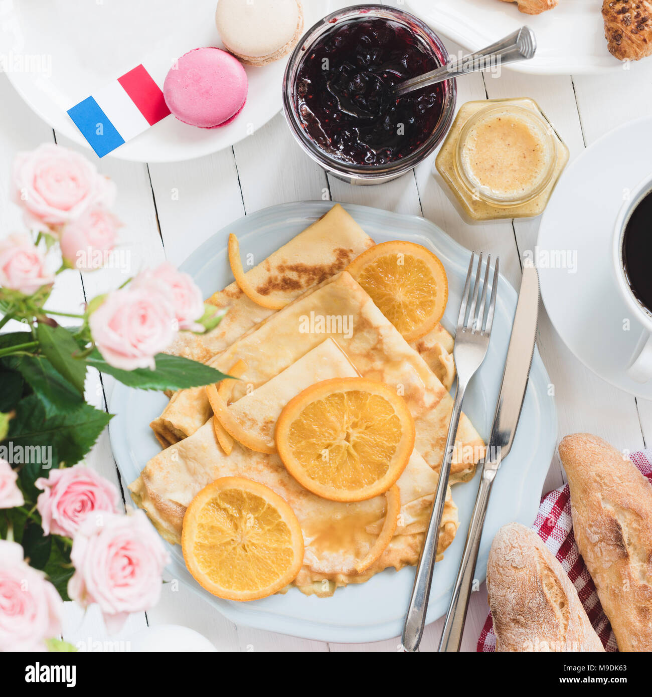 French breakfast Crepes Suzette, baguette, coffee and jam on white wooden table. French flag, macarons, jam, honey and roses aside Stock Photo