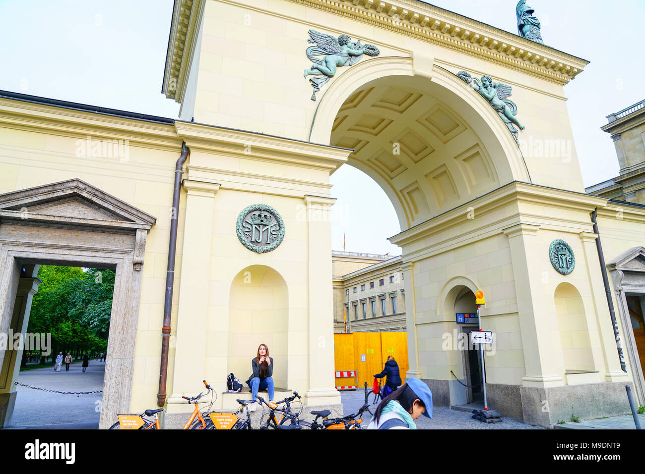 MUNICH GERMANY -SEPTEMBER 9, 2017; Ornate architectural detail  of wall and arched entrance with pretty girl sitting niche twisting hair by hire bicyc Stock Photo