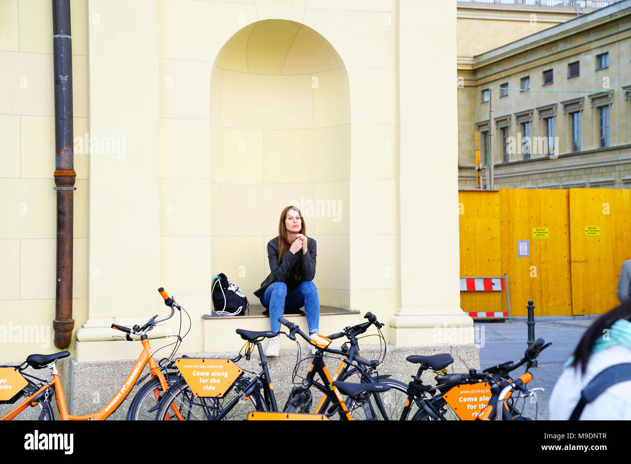 MUNICH GERMANY -SEPTEMBER 9, 2017; Pretty Girl in wall girl sitting niche twisting hair by hire bicycles. Stock Photo