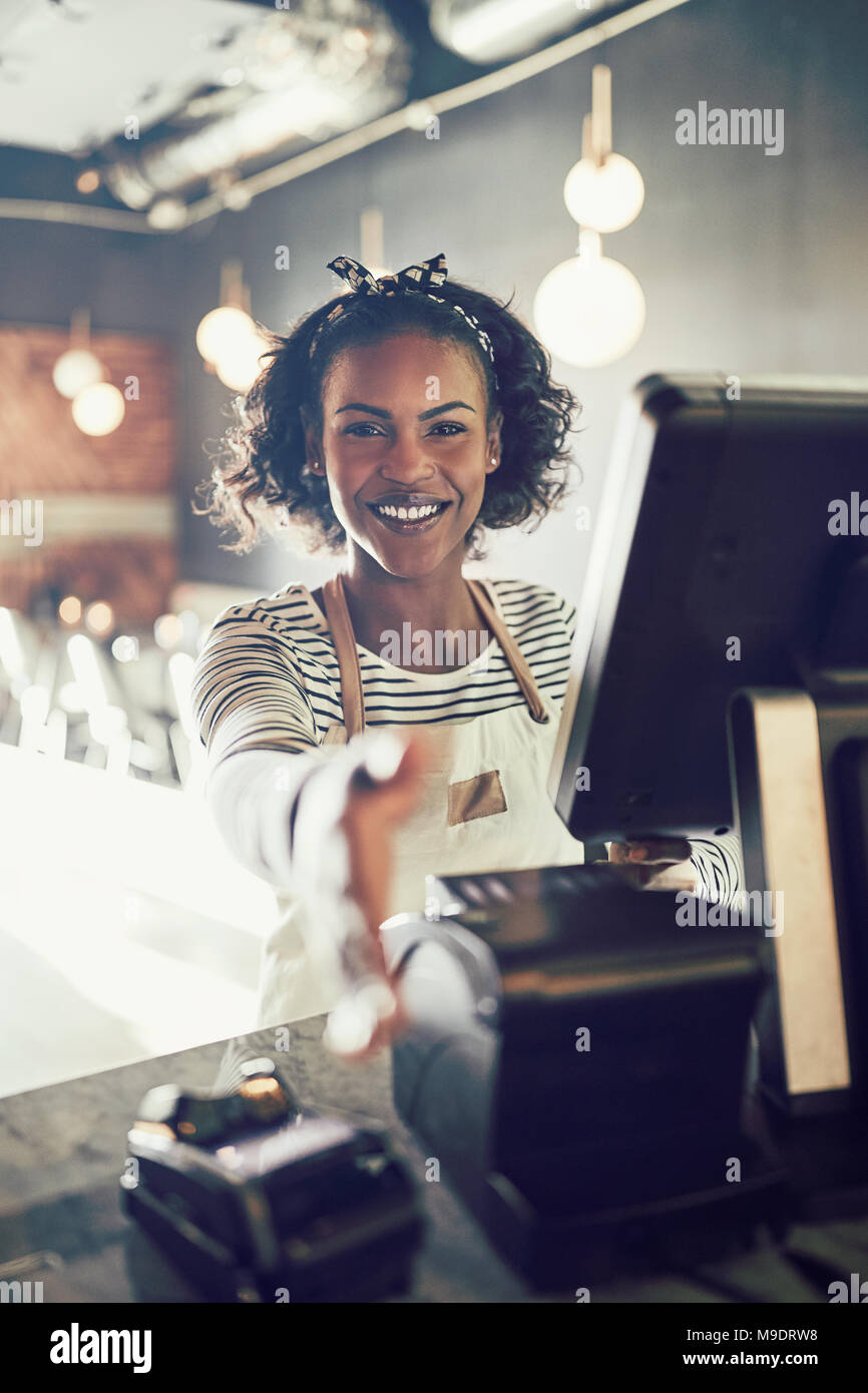 Smiling young African cafe owner standing at a point of sale terminal
