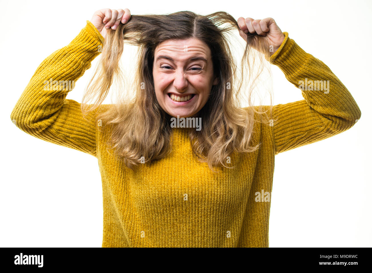 A young Caucasian woman girl wearing a yellow jumper sweater, looking frustrated and angry,  pulling her hair against a white background, UK Stock Photo