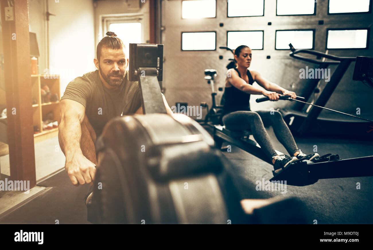 Fit young people exercising together on rowing machines during a ...