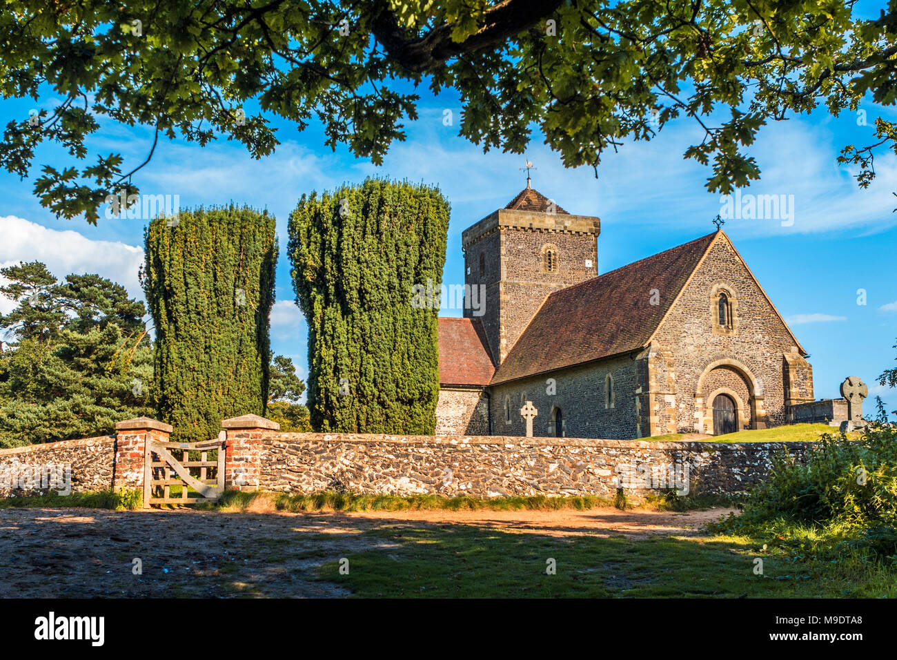 Church of St Martha-on-the-Hill in the North Downs of Surrey, Guildford, on beautiful sunny day with pruned trees, walled graveyard and gate Stock Photo