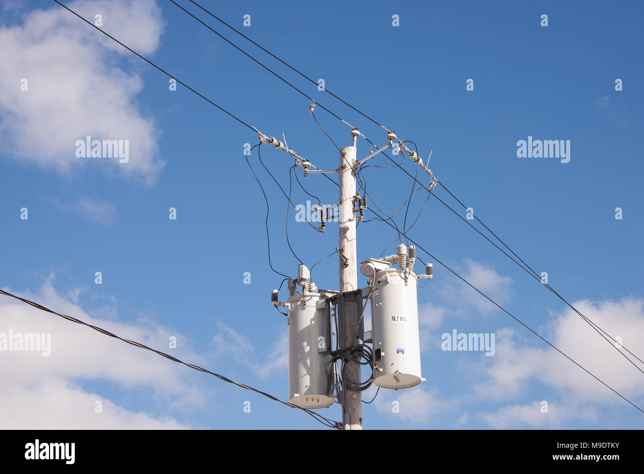 Two electric power transformers on a pole with wires, connectors and insulators with a deep blue sky and white cloud background. Stock Photo