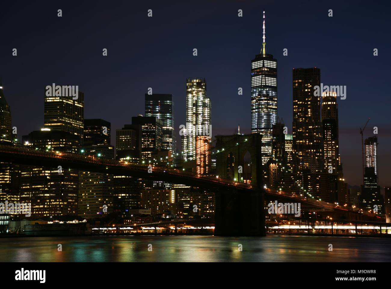 The Freedom Tower, Wall Street, and the skyline of downtown Manhattan from Brooklyn at night. Stock Photo