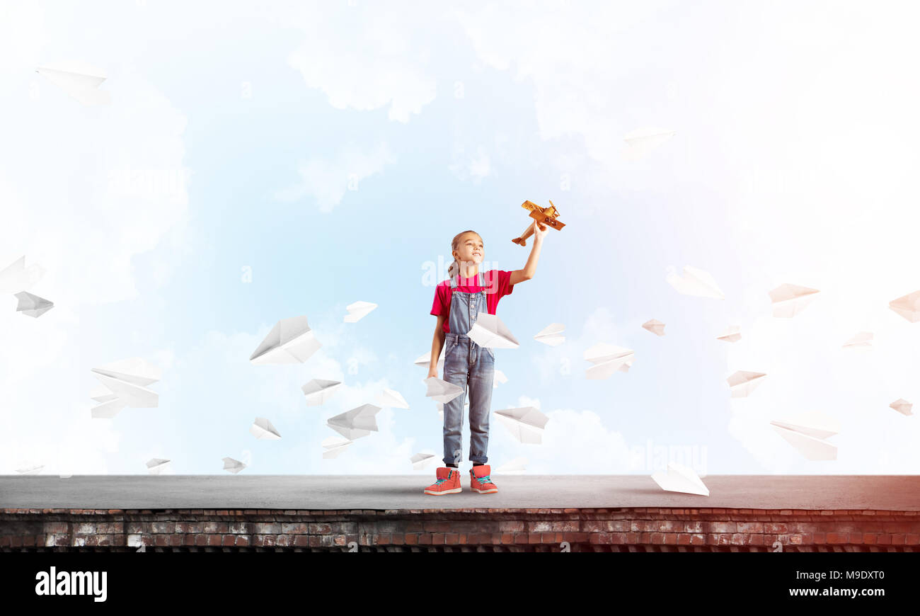 Cute happy kid girl on building top playing with retro plane model Stock Photo