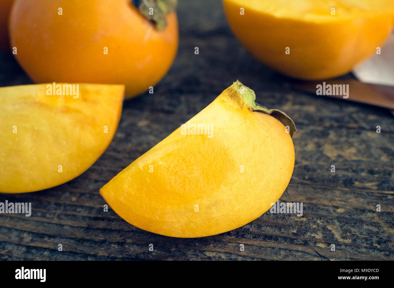 Slice of ripe delicious fresh persimmon kaki fruit on old wooden table. Stock Photo