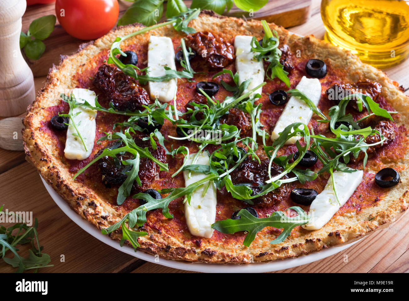 Gluten-free grain-free vegetarian pizza made from mashed cauliflower and almond flour, topped with sundried tomatoes, olives, goat cheese and fresh ar Stock Photo
