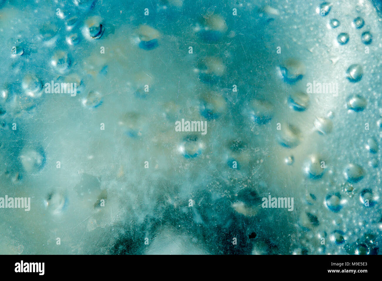 Texture of thick glass of a blue color, grunge, heavily scratched with a drops of condensed water vapor under the surface. Ground lamp abstract Stock Photo