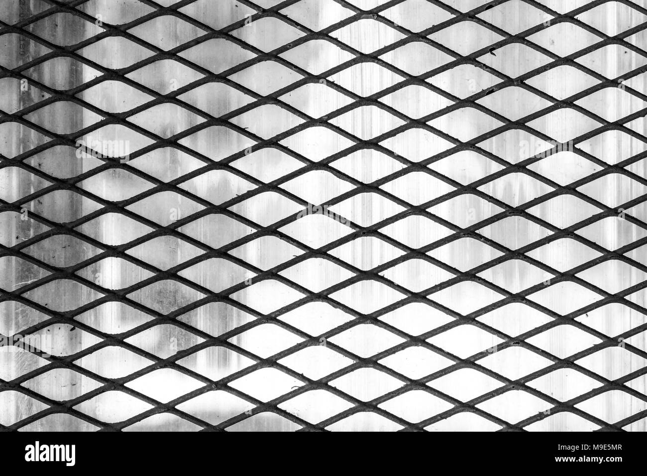 Dark metal wire protective diagonal grid or mesh, soft grey background. Black and white photo Stock Photo