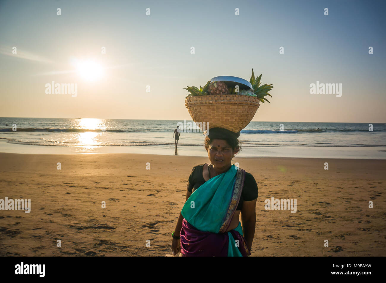 A woman with a wicker basket on his head selling fruit on the beach, India, Gokarna. Photo taken March 22, 2017. Stock Photo
