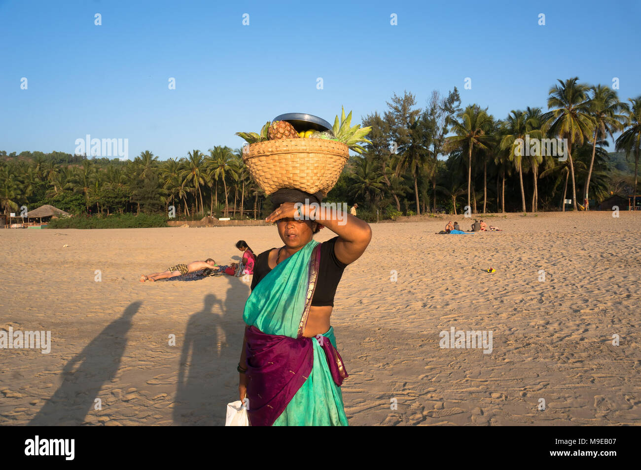 A woman with a wicker basket on his head selling fruit on the beach, India, Gokarna. Photo taken March 22, 2017. Stock Photo