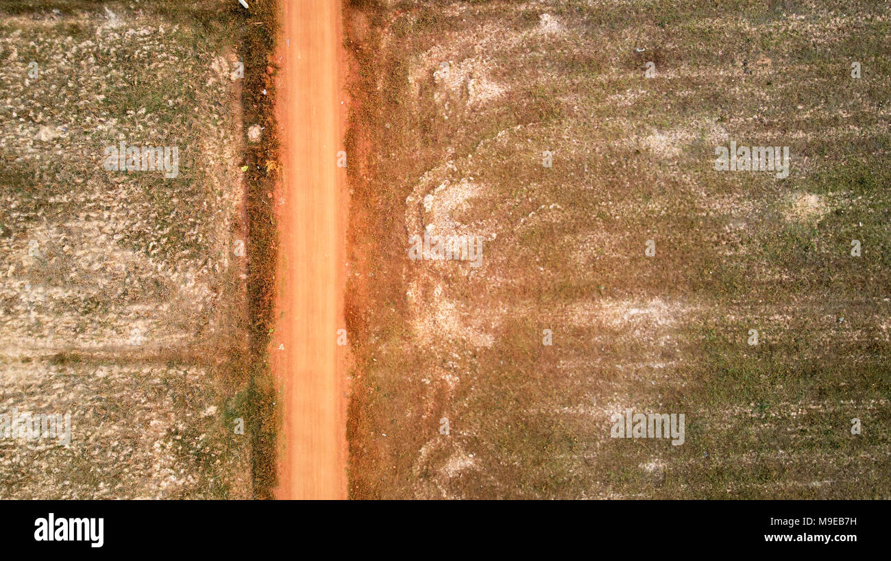 Bird eye eagle view from a drone of a red coloured road crossing rice fields in Cambodia Stock