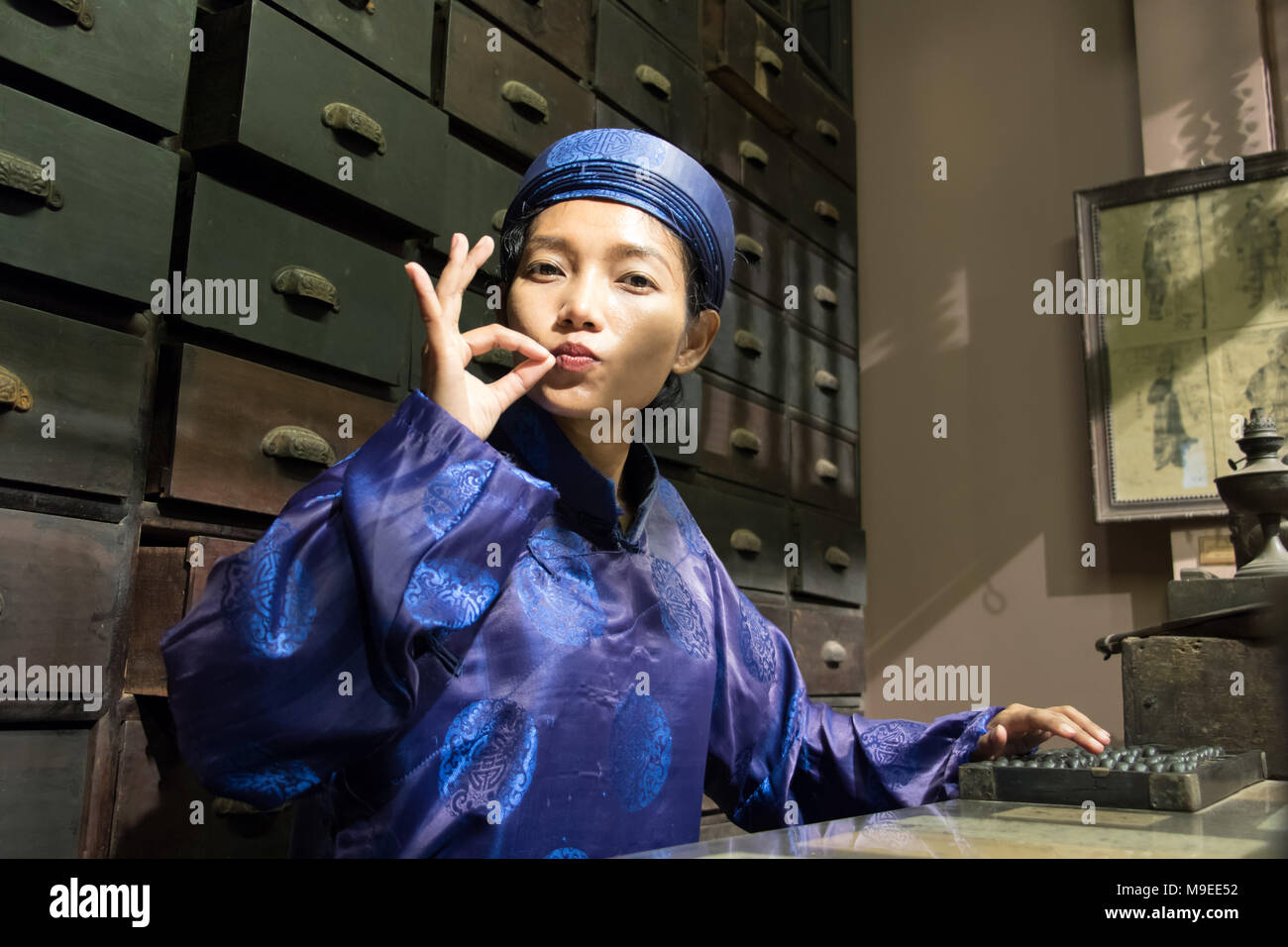 Asian pharmacist working at oriental pharmacy from the 19th century. Woman in traditional costume eastern druggist in the ancient drug store. Stock Photo