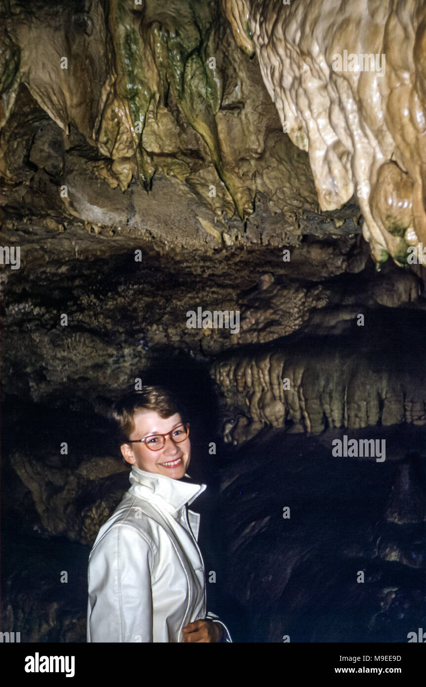 Smiling young woman wearing glasses with short hair in a dark cave with stalactites, Washington state USA in 1950s Stock Photo