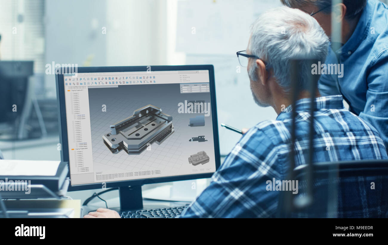 Two Senior Engineers Working With Detail Blueprint on a Personal Computer. They Actively Discuss Various Plans and Schemes. Stock Photo