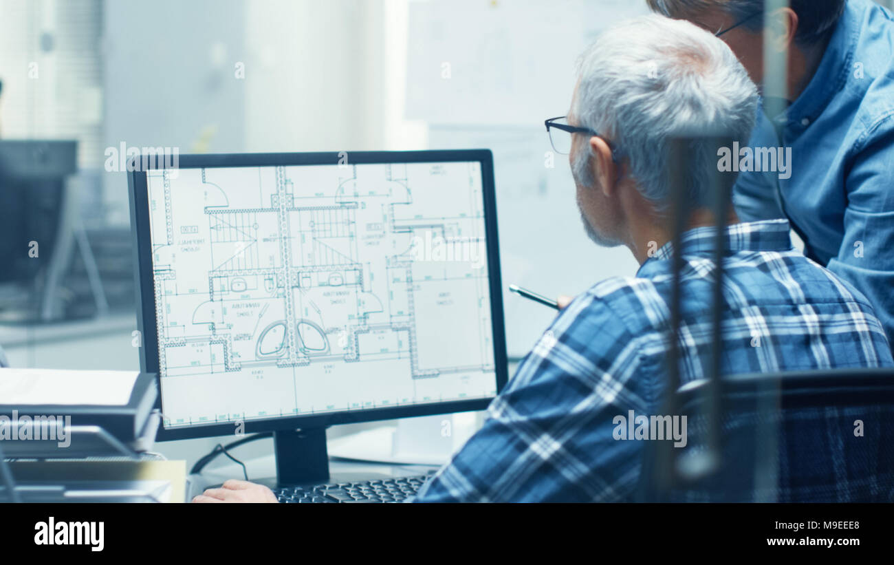 Two Senior Architectural Engineers Working With Building Blueprint on a Personal Computer. They Actively Discuss Various Plans and Schemes. Stock Photo