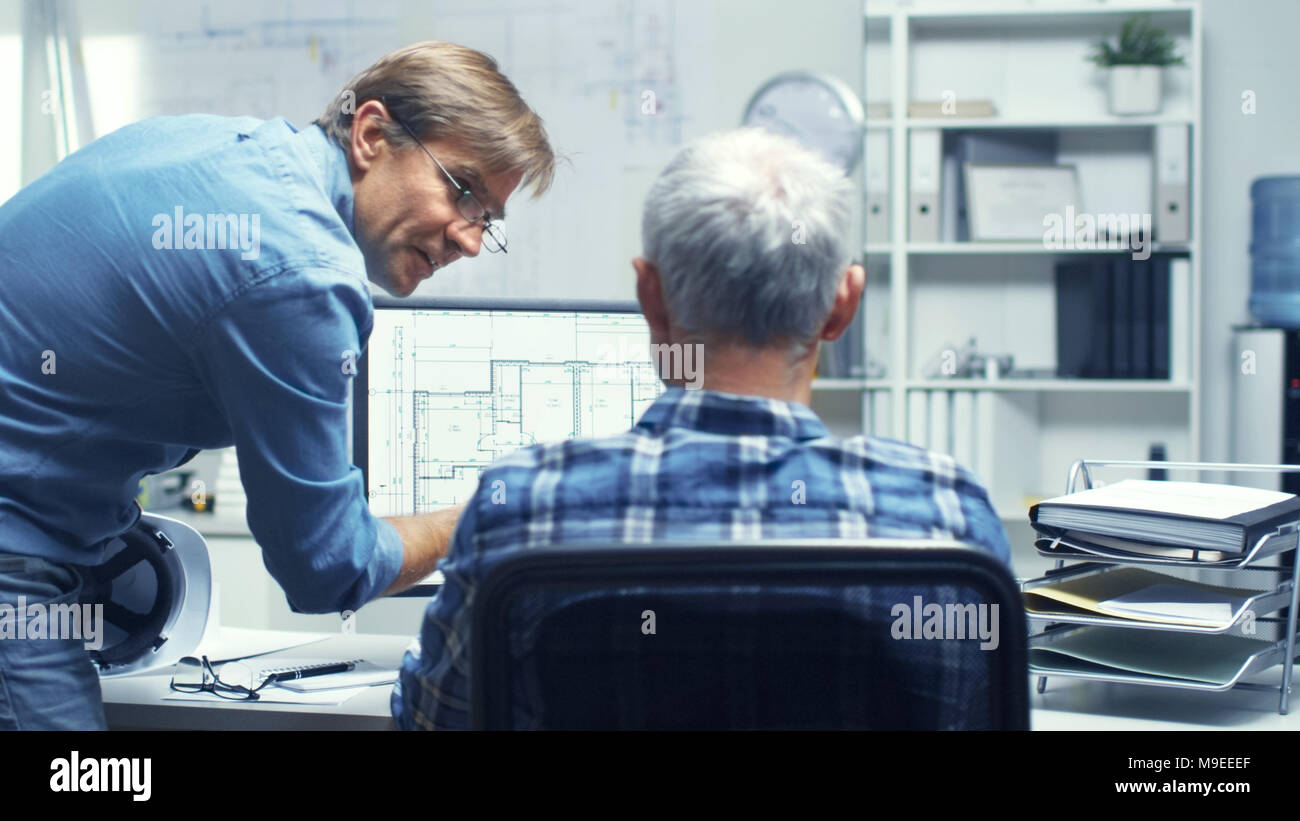 Two Senior Architectural Engineers Working With Building Plan on a Personal Computer. They Actively Discuss Various Plans and Schemes. Stock Photo