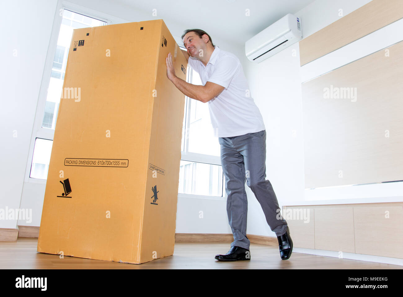 A man likes a big paper box in the apartment. A emotional man fondle a big package in the empty room. Stock Photo