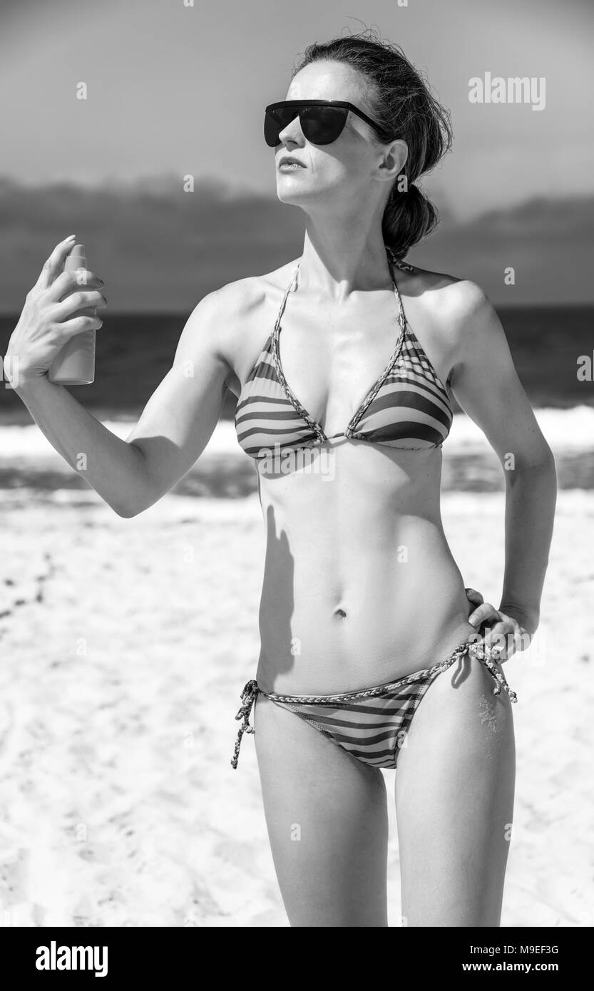 Blue sea, white sand paradise. young woman in sunglasses and bikini on the beach applying suntan lotion Stock Photo