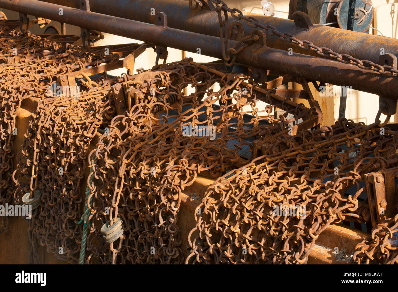Chain mat, used for raking the sea-bed to disturb scallops, nephrops and flatfish from sediment, hanging over the edge of a fishing trawler boat. Stock Photo