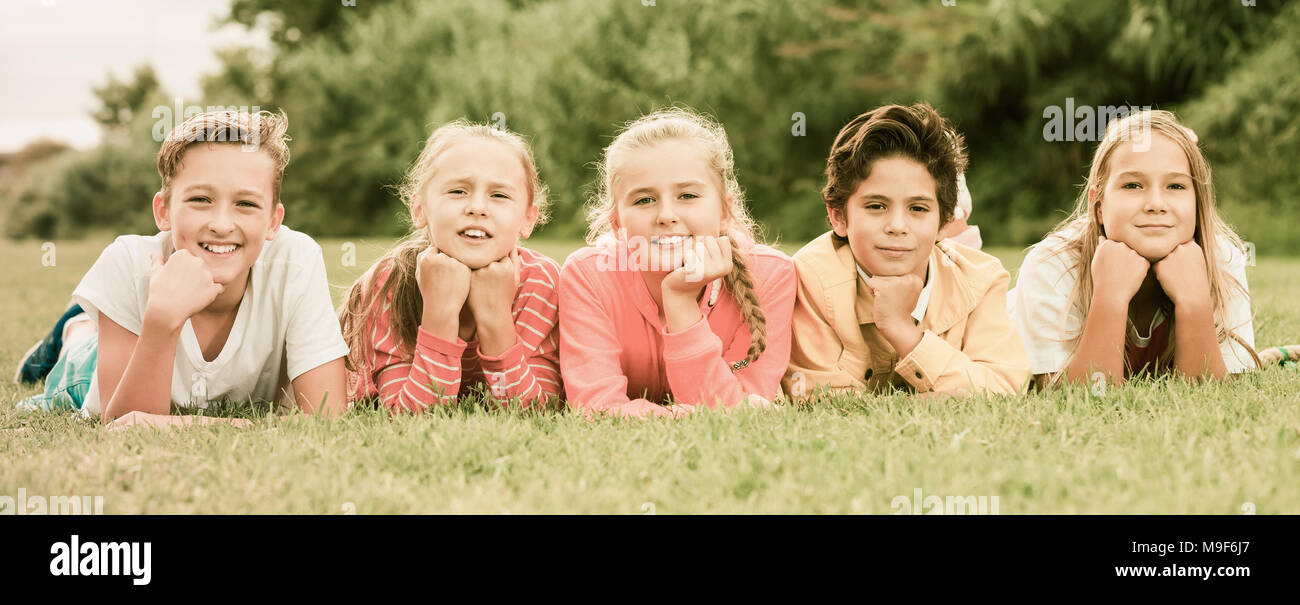 Company of five kids are posing lying on grass in the park Stock Photo ...