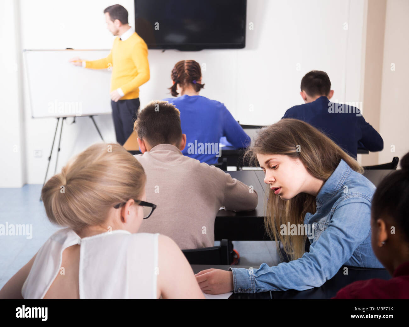 Female student is cheating on and looking test answers in her neighbor’s work. Stock Photo