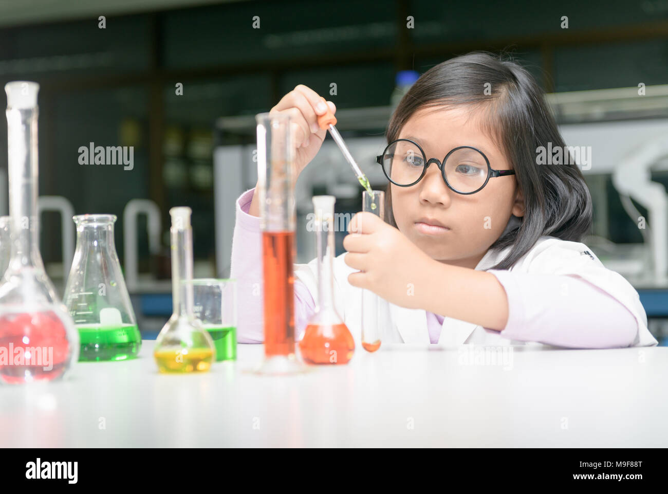 Excited little girl in lab coat making experiment with test tube in ...