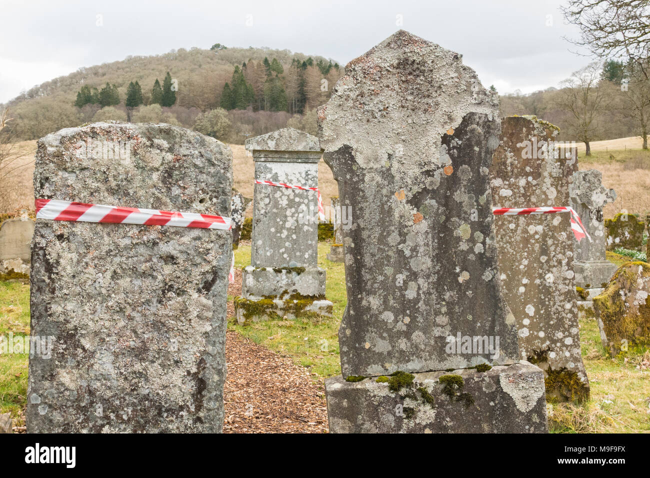 memorial safety - red and white hazard warning tape wrapped around headstones in Aberfoyle Old Parish Churchyard, Scotland, UK Stock Photo