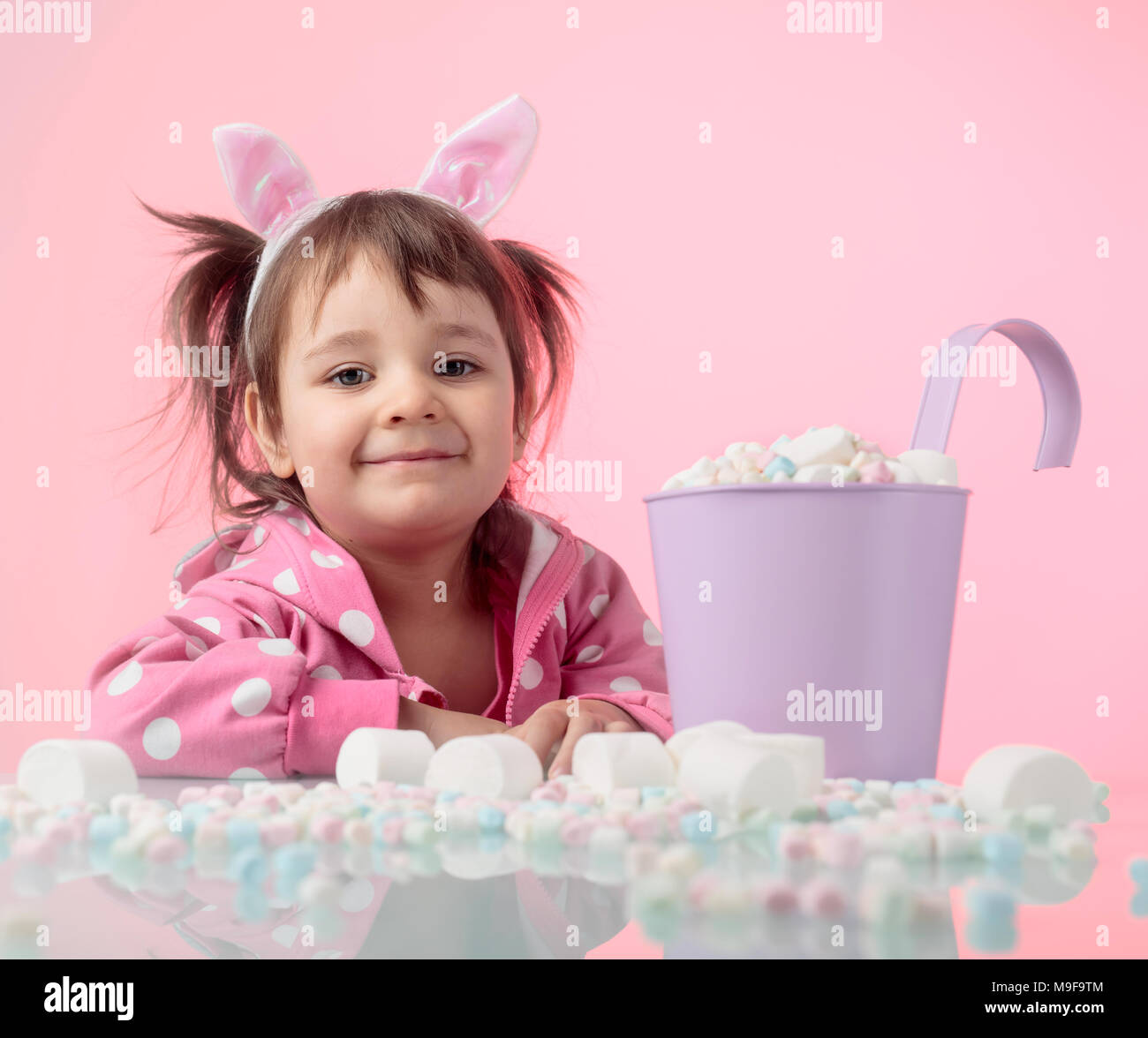 Portrait of a cute little girl with marshmallow, isolated over pink background. Expressive facial expressions. Copy space for your text. Stock Photo