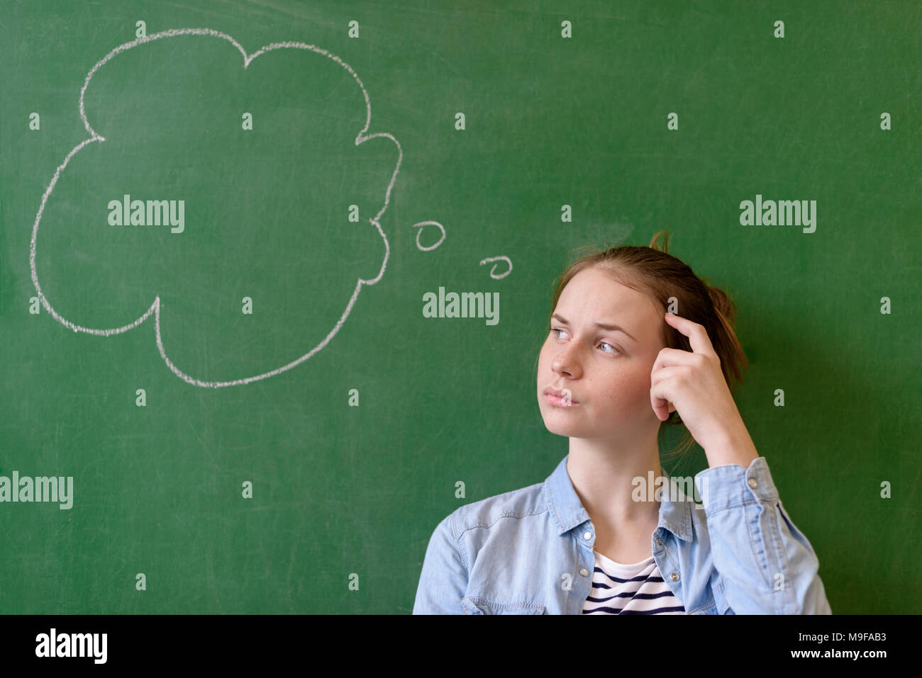 Student thinking blackboard concept. Pensive girl looking at thought bubble on chalkboard background. Caucasian student. Stock Photo