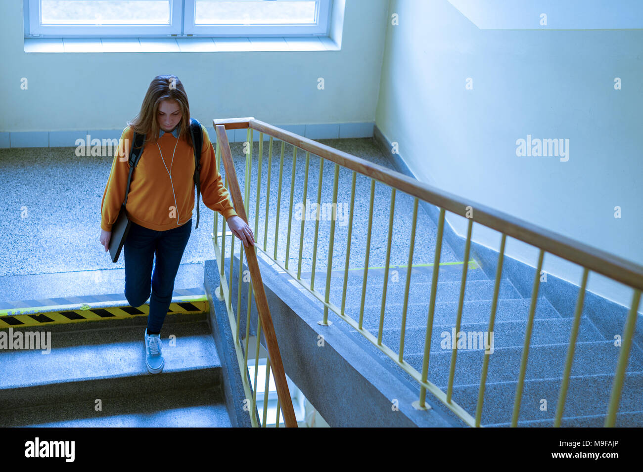 Young depressed lonely female college student walking down the stairs at her school, looking down. Education, Bullying, Depression concept. Stock Photo