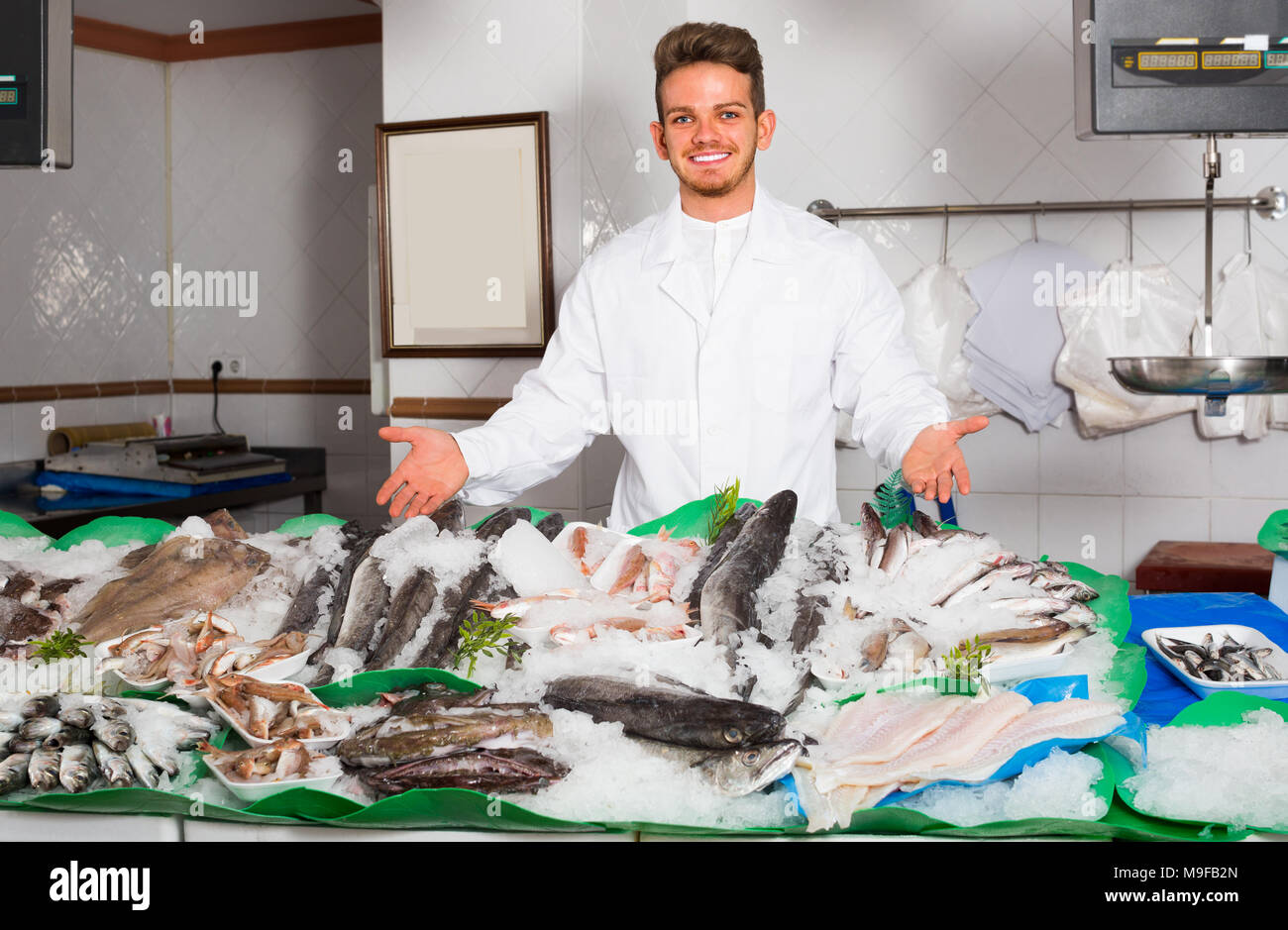 Young positive salesman with apron offering fresh fish in shop Stock ...