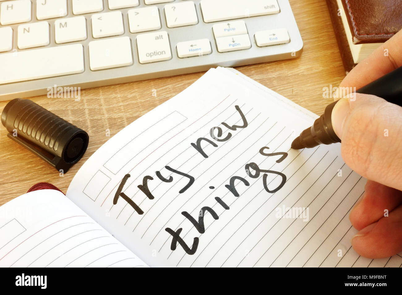Man writing: try new things in a note. Stock Photo