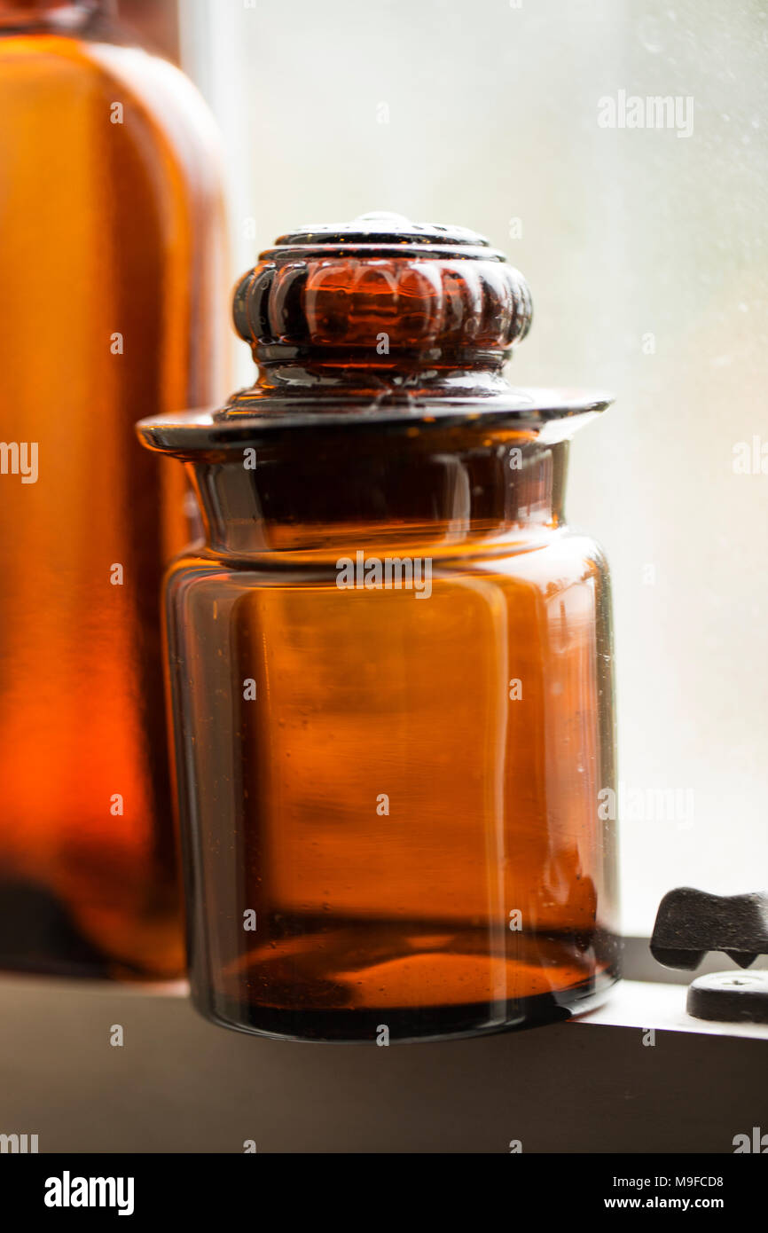An antique amber glass bottle with an ornate lid, sitting on a window sill. Stock Photo