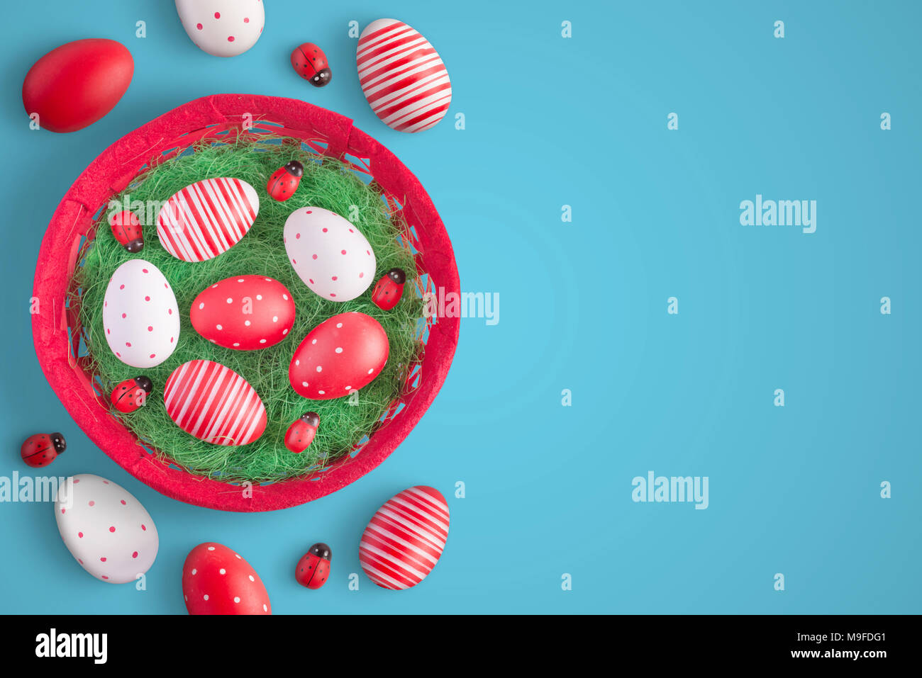 Easter eggs in red basket with ladybug decorations. Top view of blue surface with free space for text. Stock Photo