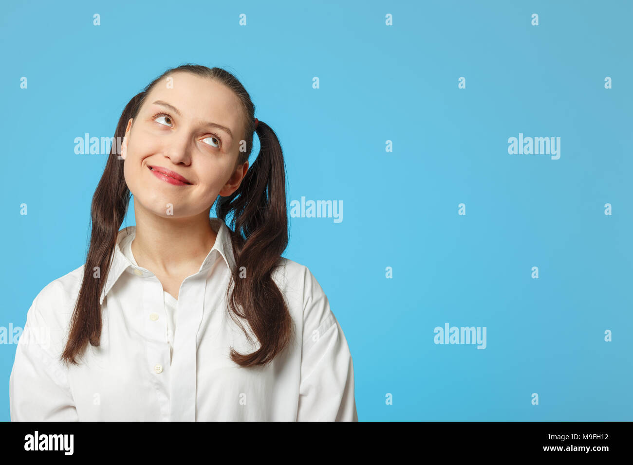 fun girl thinker on blue background with copy space looking up Stock