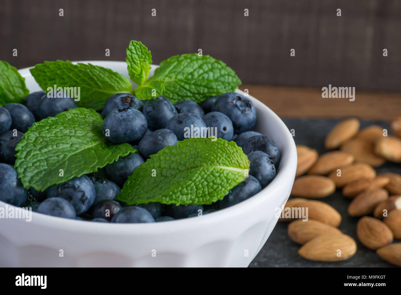 Ready for Summer Fruit? Raw, sweet blueberries in a white bowl look beautiful and taste even better. Lemon and mint add a bright contrast of color. Stock Photo