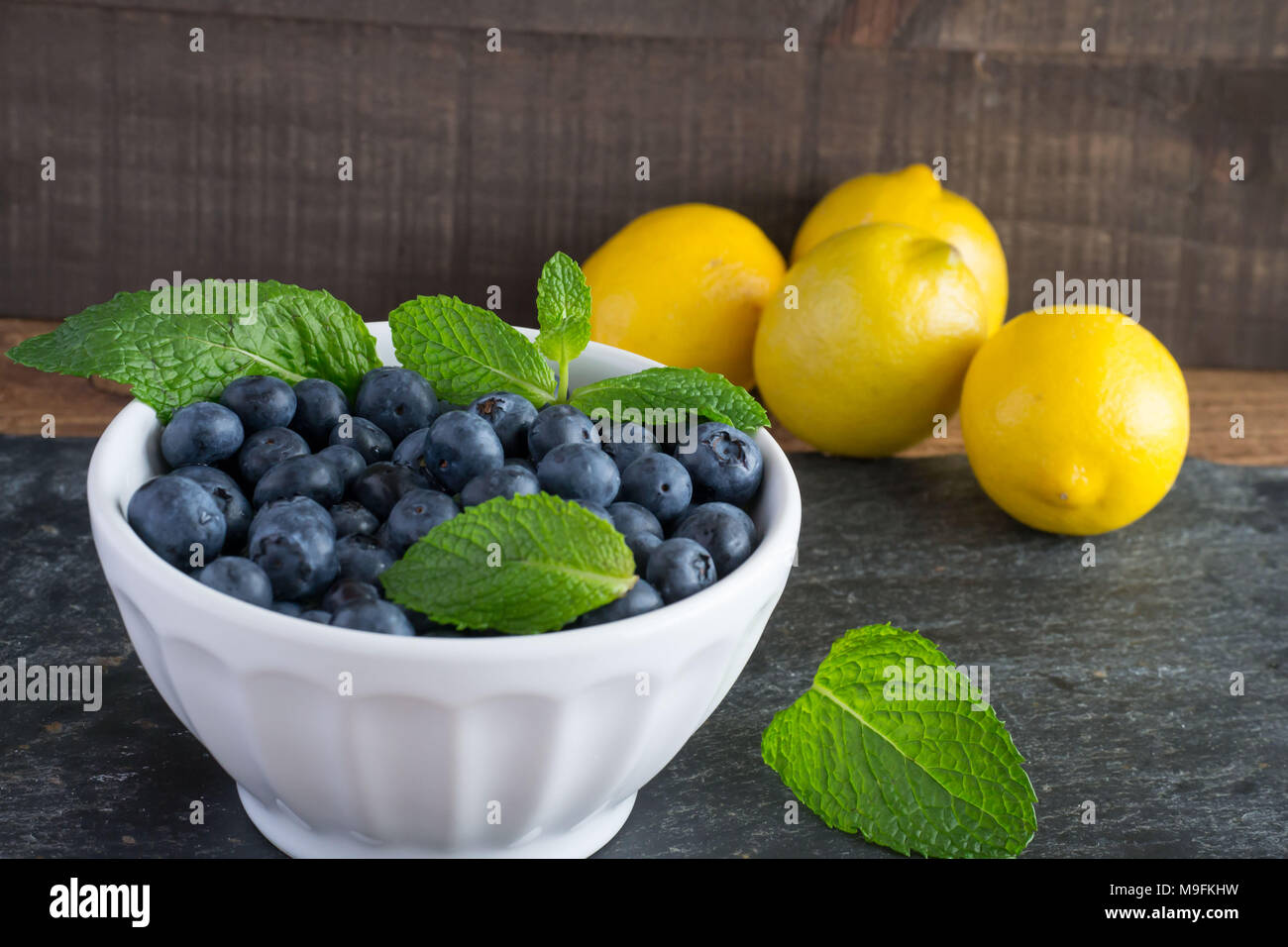 Ready for Summer Fruit? Raw, sweet blueberries in a white bowl look beautiful and taste even better. Lemon and mint add a bright contrast of color. Stock Photo