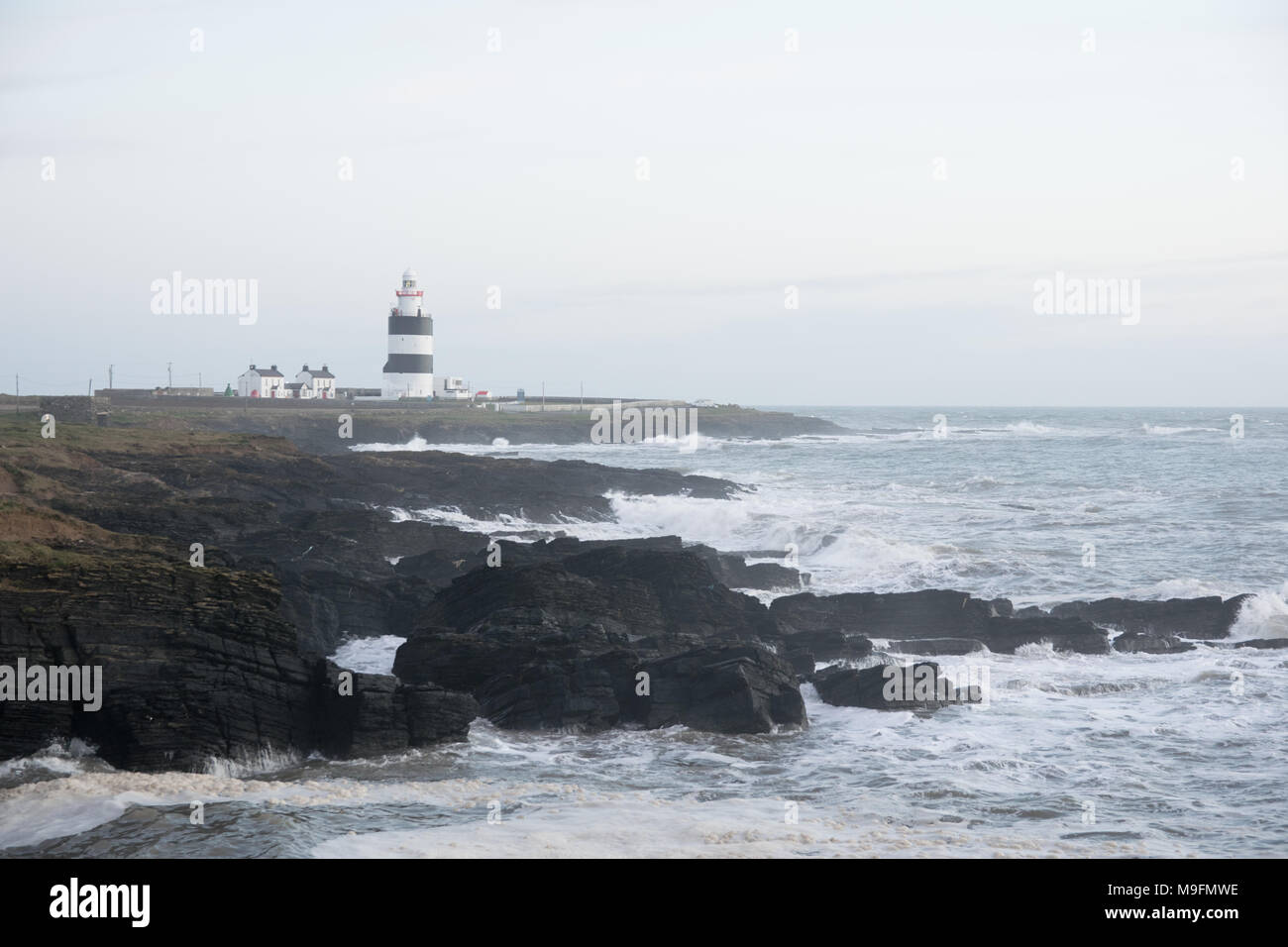 Irish light house on a rocky coastline with waves crashing up ion the shore. Stock Photo
