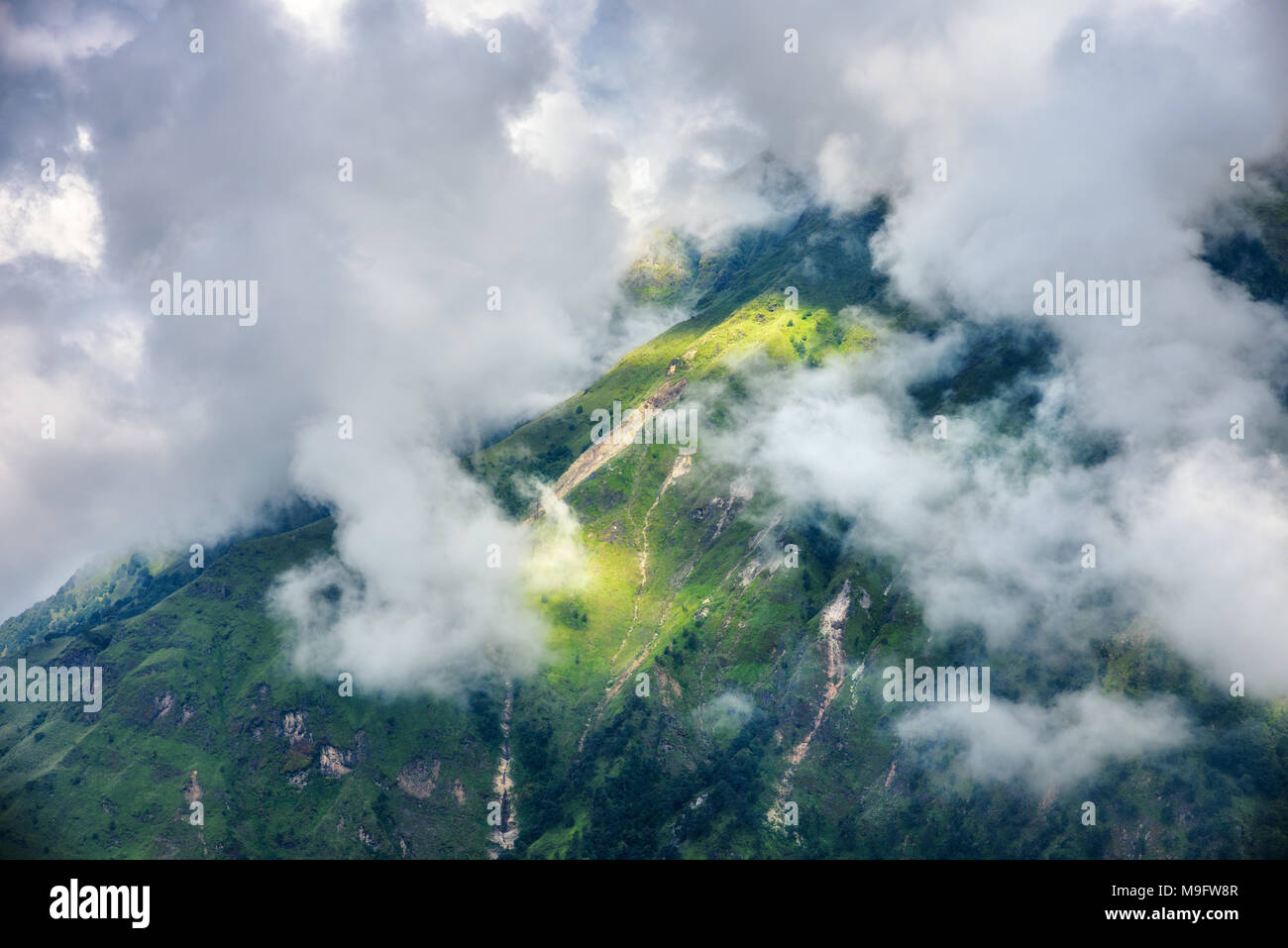 Mountains with green forest in clouds in overcast day in summer in Nepal. Landscape with beautiful hills with trees and dramatic cloudy sky at sunset. Stock Photo